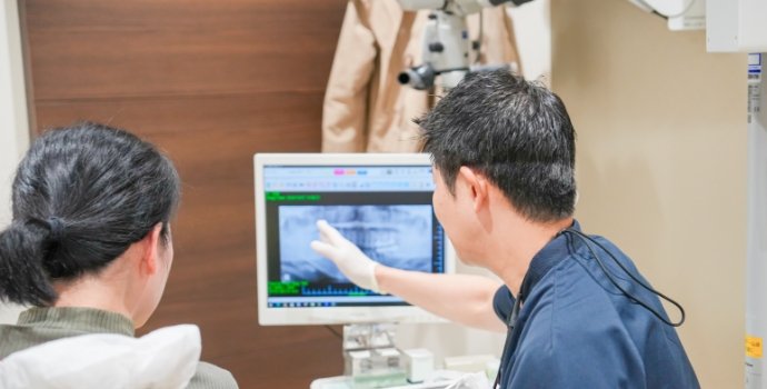 モニターのレントゲン画像を指しながら，患者さまに説明する院長